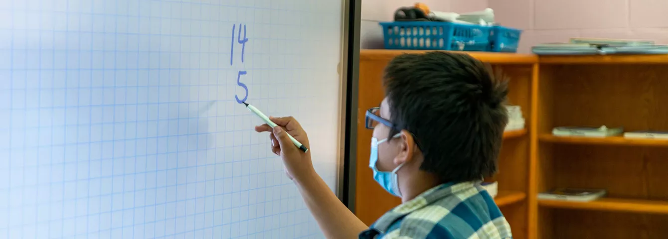 Male student doing a math problem on a digital board.