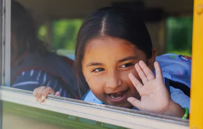 Young female student waving out the school bus window.