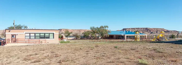 Lake Valley Navajo School exterior building view with yellow playground to the right and scenic mountain in the background. 