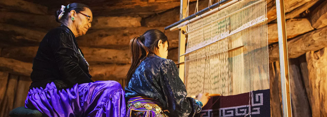An adult woman showing a young girl how to weave using a weaving loom.