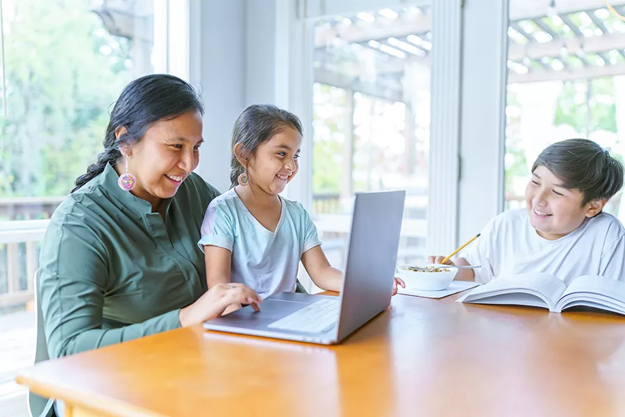 Parent helping children with school work at the kitchen table.