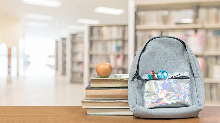Backpack beside a stack of books topped with an apple.