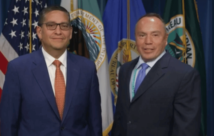 Billy Kirkland and Director Dearman stand side by side in front of U.S. and state government flags.