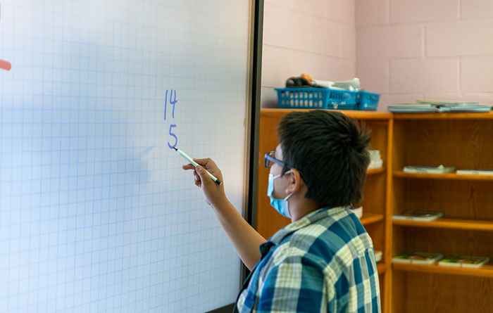 Young boy doing a math problem on the digital board.