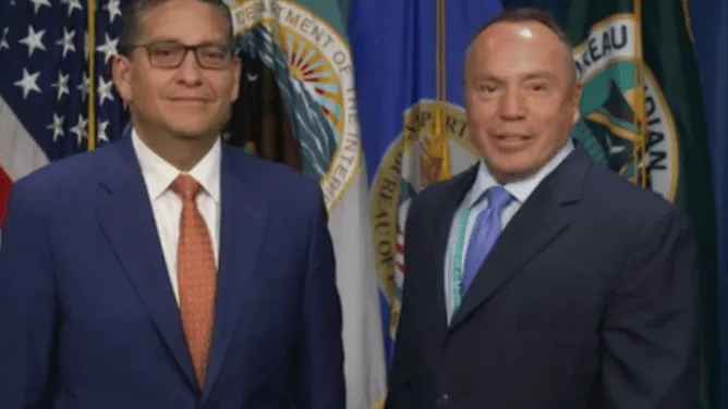 Billy Kirkland and Director Dearman stand side by side in front of U.S. and state government flags.